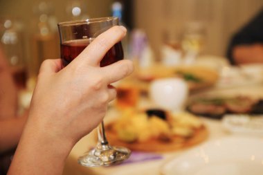 Kadının eli masada bir bardak kırmızı şarap tutuyor..