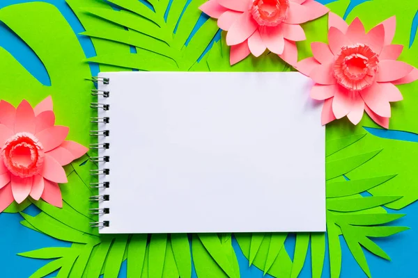 Concept hello summer. Notepad on palm tree leaves and tropical flowers. Paper art. Top view background. Flat lay. copyspace. Empty.