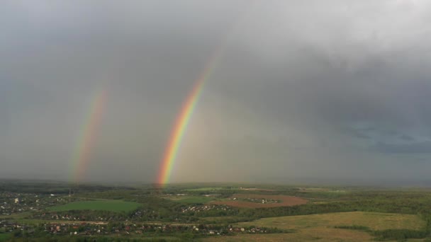 Antenn utsikt över en dubbel regnbåge på himlen under regn, regnbåge över byar och gröna fält — Stockvideo