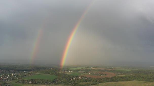 Antenn utsikt över en dubbel regnbåge på himlen under regn, regnbåge över byar och gröna fält — Stockvideo