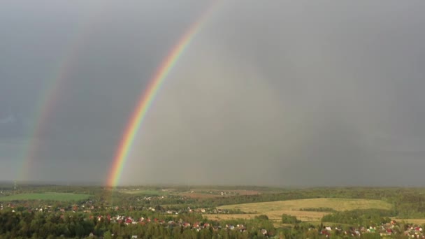 Воздушный вид двойной радуги в небе во время дождя, радуги над деревнями и зелеными полями — стоковое видео