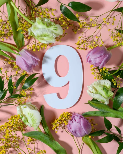Renkli çiçeklerle pembe arka planda dokuz numara. Düz yatış, üst görünüm.