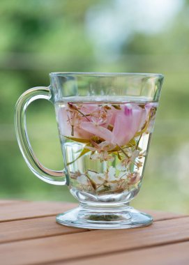 Bitkisel rugosa gülü (Rosa rugosa, Japon gülü), ahşap masadaki cam fincanda çay.