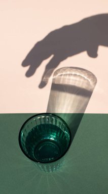 Sert camlı yeşil içki bardağı ve renkli arka planda insan eli gölgeleri. Kapat..