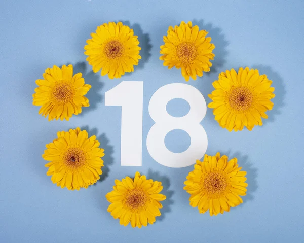 Número 18 rodeado de flores de gerberas amarillas sobre fondo azul. — Foto de Stock