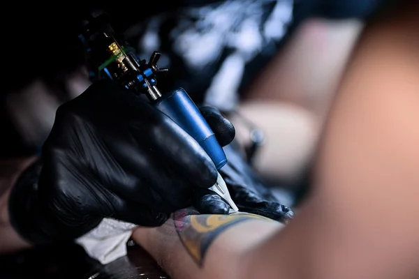 Tattoo kunstenaar waardoor tatoeage. Meesterwerken op professionele machine en in steriele zwarte handschoenen. — Stockfoto