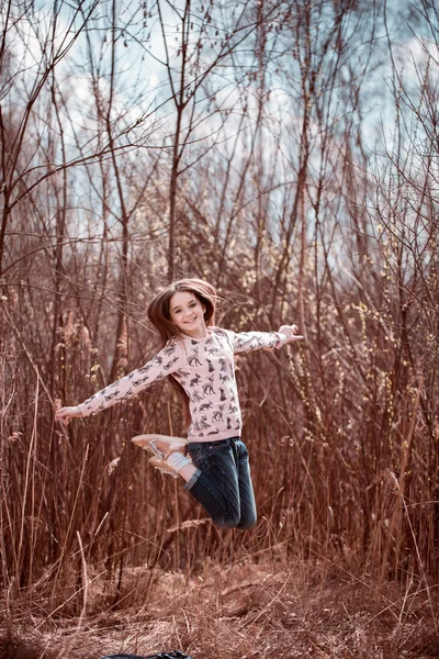 Garota sorridente pulando na grama no prado. A olhar para a câmara. Infância. De volta à escola . — Fotografia de Stock
