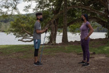 Gençler jartiyer ile gölün kıyısında egzersiz yapıyorlar.