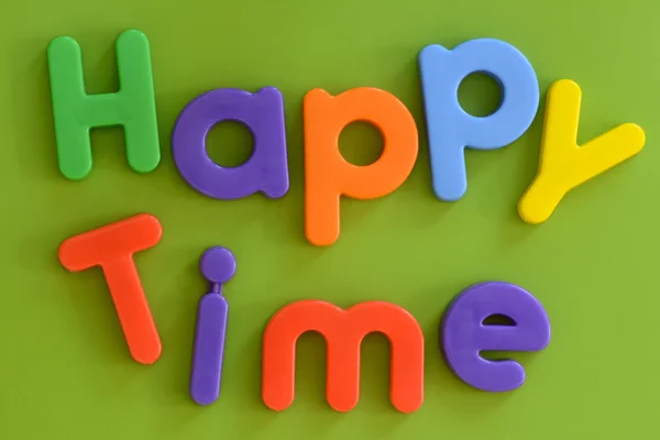 Worte glückliche Zeit, in bunten Plastikbuchstaben auf grünem Hintergrund — Stockfoto