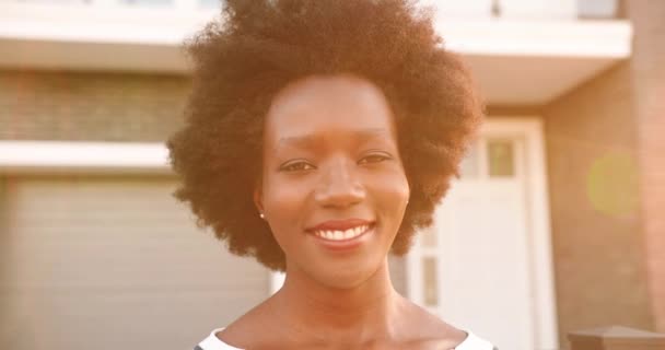Portrait de belle jeune femme afro-américaine souriante avec des cheveux bouclés regardant la caméra en plein air à la maison. Gros plan du visage d'une jolie fille joyeuse souriant joyeusement sincèrement à la rue. — Video