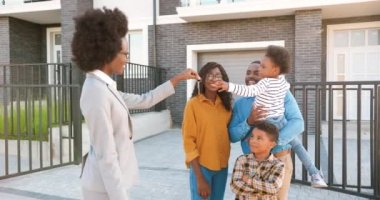 Afrikalı mutlu çocuklu Amerikan ailesine ev satan kadın emlakçı. Anahtarları veriyorum. Açık havada. Neşeli bir adam ve çocuklu bir kadın varoştan ev alıyor. Banliyöde konaklama.