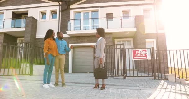 African American young woman real-eastate agent selling house to happy just-married couple. Outdoor. Wealthy man and woman buying dwelling in suburb. Businesswoman talking with new neighbors. — Stock Video