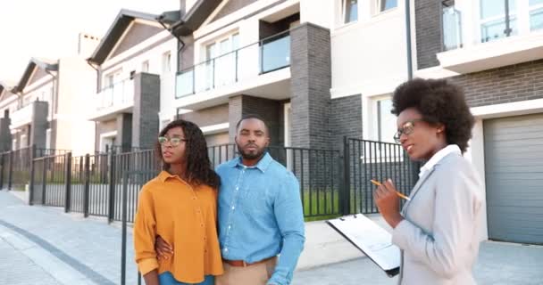 Jeune femme afro-américaine agent immobilier vendant la maison et parlant à un couple marié heureux. En plein air. Un homme et une femme riches achetant un logement en banlieue. Femme d'affaires parlant de quartier — Video