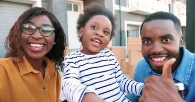 Afro-Amerikan neşeli aile portresi. Dışarıda video sohbeti yaparken kameraya gülümseyen ve konuşan küçük tatlı bir kız. Gülümseyen mutlu anne, baba ve küçük kız webcam üzerinden sohbet ediyorlardı. Video Hattı.