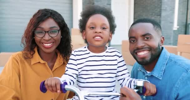 Ritratto di giovane famiglia afroamericana felice con piccola ragazza carina in bicicletta sorridente alla macchina fotografica all'aperto. Gioioso sorriso madre e padre con la piccola figlia in bicicletta. — Video Stock