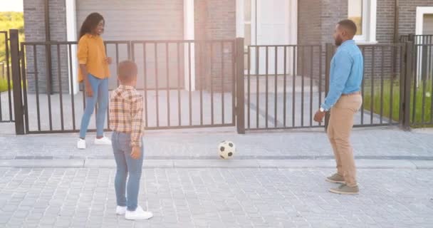 I genitori afroamericani giocano a calcio con il piccolo figlio carino all'aperto in casa in periferia. Felice allegra famiglia giocare gioco di sport in strada in estate. Madre, padre e bambino si divertono. — Video Stock