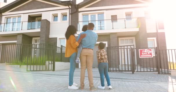 Back view on happy African American family with small children standing at new house at suburb and looking on it. Rear on cheerful parents and kids moving in new home. Settlement in outskirt. Sold. — Stock Video