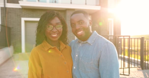 Portrait de heureux jeunes afro-américains mariés debout à la cour de la maison, étreignant et souriant à la caméra. homme gai et femme dans les câlins déménageant dans une nouvelle maison. — Video