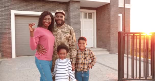 Πορτρέτο της Αφροαμερικανικής οικογένειας αξιωματικού του στρατού με μικρά παιδιά που μετακομίζουν σε νέο σπίτι και δείχνουν τα κλειδιά. Εξωτερικά στην αυλή στο σπίτι. Μητέρα, πατέρας στρατιώτης, γιος και κόρη επιδεικνύουν το κλειδί. — Αρχείο Βίντεο