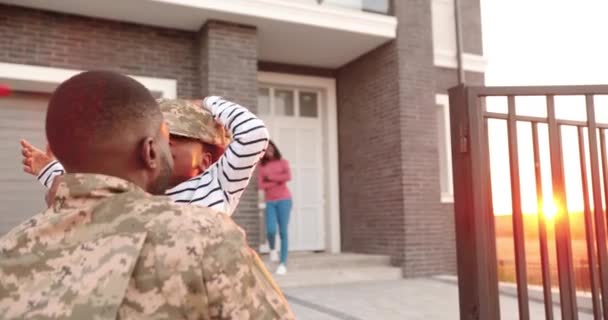 Gelukkige Afro-Amerikaanse vrouw met klein kind die man na man ontmoet in het buitenhuis van het leger in de buitenwijk. man soldaat komt terug naar huis naar familie en spelen met leuke dochter. — Stockvideo