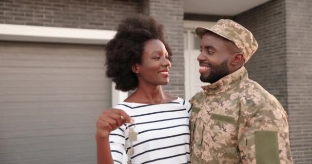 Portret van jonge Afro-Amerikaanse getrouwde soldaten die thuis in knuffels staan, glimlachend en met de sleutel tot de camera. Man in uniform met vrouw in een nieuw huis. Onroerend goed — Stockvideo