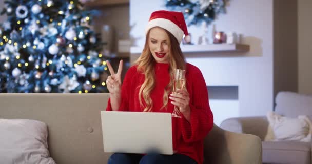 Szczęśliwa młoda, piękna biała kobieta w kapeluszu Mikołaja w urządzonym pokoju ze świecącą choinką rozmawiająca przez telefon wideo online na laptopie i uśmiechnięta święta Bożego Narodzenia. Uroczysty nastrój. Koncepcja nowego roku — Wideo stockowe