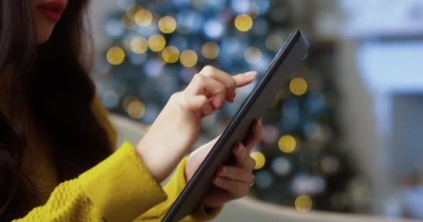 Primer plano de asiático bastante joven morena hembra buscando internet y tocando en la tableta en casa cerca de árbol brillante decorado. Mujer manos escribiendo en línea en el dispositivo. Concepto de comercio electrónico — Vídeos de Stock