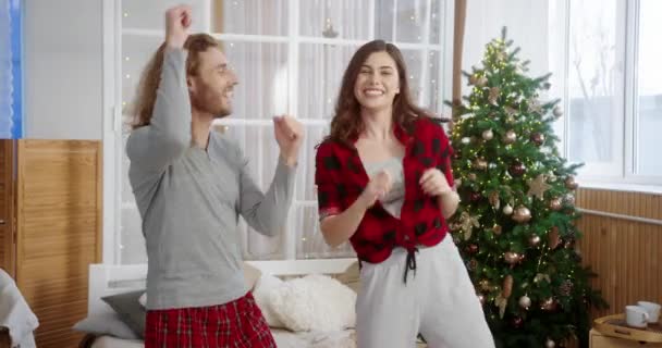 Portrait of Caucasian cheerful young married couple having fun and dancing at cozy home near glowing decorated xmas tree celebrating New Year. Christmas celebration. family concept — Stock Video