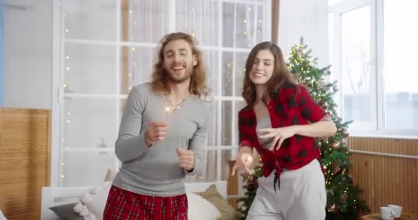 Portret van Kaukasisch gelukkig jong koppel vrouw en echtgenoot met sterretjes die plezier hebben en dansen in gezellig huis in de buurt van gloeiende versierde kerstboom vieren Nieuwjaar. Kerstfeest — Stockvideo