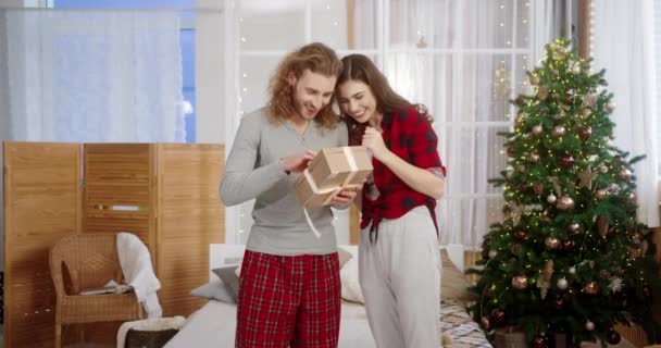 Счастливый удивленный молодой кавказский муж, стоящий у украшенного дома, получает рождественскую подарочную коробку от заботливой любящей жены и открытый подарок в канун Нового года. Концепция праздника — стоковое видео