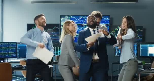 Happy funny cheerful mixed-races male and female traders dancing, having fun and tossing documents after long hard working day. Multiethnic men and women colleagues celebrating successful trading. — Stock Video