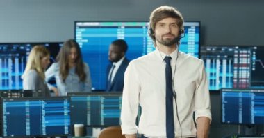 Borsa ofisinde kameraya gülümseyen kravatlı ve kulaklıklı yakışıklı beyaz adamın portresi. Ticaret konsepti. Monitörleri ve bilgisayarları olan profesyonel bir tüccar. Satış yöneticisi.