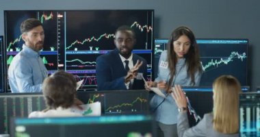 Borsadaki çok ırklı kadın ve erkek tüccarlar borsada konuşuyorlar ve değiş tokuş oranlarını tartışıyorlar. Karışık ırk simsarları, ticaret ofisinde tartışıyor, alıp satıyor. Grafikli ve oranlı monitörler.