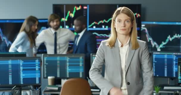 Retrato de una hermosa mujer caucásica mirando a la cámara y cruzando las manos en la oficina de bolsa. Concepto comercial. Comerciante femenina profesional en la habitación con monitores y computadoras. Gerente de ventas. — Vídeo de stock