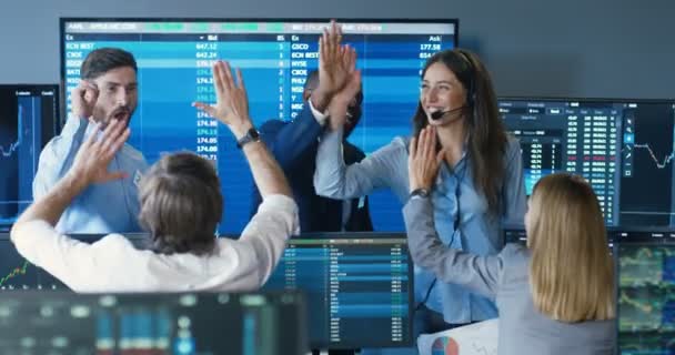 Mixed-races happy cheerful males and females brokers smiling and giving fives to each other after suceess in trading. Exchange office with monitors and rates. Multietnic traders celebrating. — Stock Video