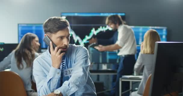 Blanc beau courtier masculin travaillant à l'ordinateur dans le bureau commercial et répondre aux appels téléphoniques sur de nombreux téléphones. Trader acheter et vendre tout en parlant avec les clients et travailler dur. Travail commercial. — Video