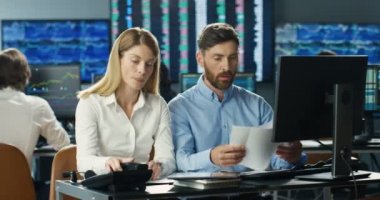 İş ortakları modern ofiste masa başında oturmuş bazı belgeleri tartışıyorlar. İş adamı ve iş kadını bilgisayar monitöründe birlikte çalışıyor. Ticaret müdürleri. Para yatırımı.