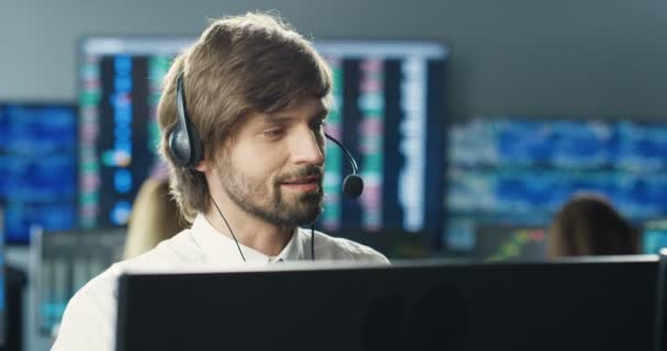 Przystojny, biały młodzieniec w brokerze pracujący na monitorze komputera i rozmawiający z klientem. Mężczyzna giełda handlowiec rozmawia przez telefon w biurze handlowym i sprzedaży. Dział sprzedaży. — Wideo stockowe
