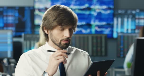Közelkép fiatal kaukázusi jóképű férfi bróker nyakkendőben ül az irodában, dolgozik tabletta eszköz és amelynek kemény munkanap. Fáradt depressziós ember befektető. Kereskedő a számítógépen problémákkal. — Stock videók