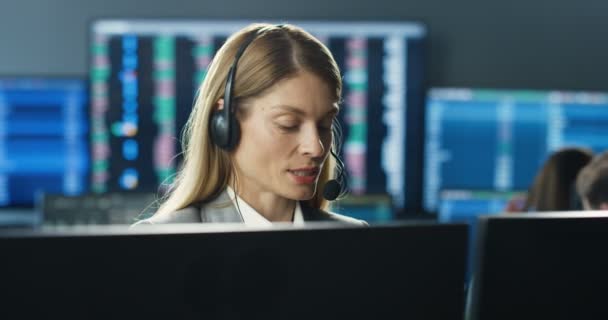 Kaukasiska unga kvinna i headset mäklare arbetar på bildskärm dator och tala med klienten. Kvinnlig börshandlare talar i telefon på handelskontoret och säljer. Försäljningsavdelningen. Anropscentral. — Stockvideo