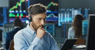 Düşünürken ve ticaret ofisinde çalışırken tablet cihaz kullanan yakışıklı, beyaz kulaklı bir tüccar. Erkek komisyoncu bahis oynuyor, satıyor ve internetten alıyor..