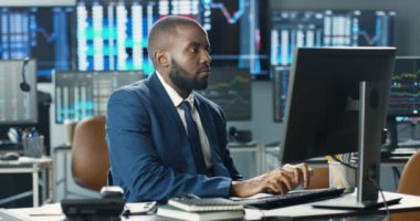 Takım elbiseli ve kravatlı yakışıklı Afrikalı Amerikalı. Bilgisayar monitöründe çalışan ve klavyede yazı yazan bir broker. Erkek müdür ticaret ofisinde mesajlaşıyor. Satış departmanı. Hisse satışı.