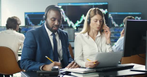 Mieszane rasy dwóch handlarzy mężczyzn i kobiet pracujących razem w słuchawkach przy biurku z komputerem i rozmawiających z klientami. Biuro Handlowe. Wieloetniczny mężczyzna i kobieta w call center. Praca maklerów — Wideo stockowe