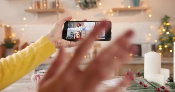 Primo piano dello schermo dello smartphone con videochiamata multipla con amiche e parenti femminili multietnici asiatici e caucasici in mano donna a Capodanno a casa decorata. Buon Natale a tutti! — Video Stock