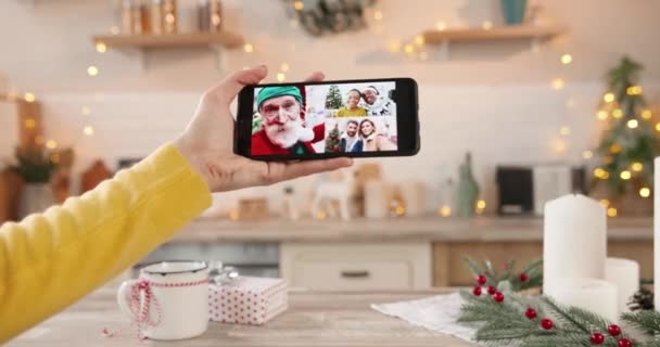 Gros plan du téléphone cellulaire avec vidéo de conférence en ligne avec des gens métis. Vidéochat avec des amis afro-américains et vieil homme caucasien en costume de père Noël. Concept de chat vidéo multiple — Video