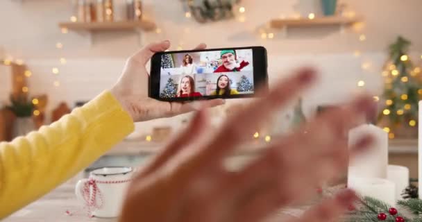 Gros plan du téléphone cellulaire avec vidéo de conférence en ligne avec différentes personnes. Vidéochat avec des amies et vieil homme caucasien en costume de Père Noël la veille de Noël. Concept de chat vidéo multiple — Video