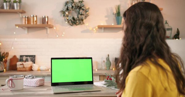 Over shoulder view. Close up of Caucasian woman in decorated home looking at screen on laptop with green screen in xmas festive period. Computer with chroma key. Technology concept Stock Photo