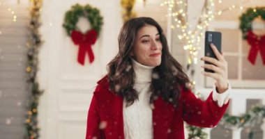 Kırmızı ceketli mutlu beyaz bir kadının portresi. Karlı bir şehirde dikiliyor ve akıllı telefondan şen şakrak konuşuyor. - Mutlu yıllar. Tatil kutlamaları