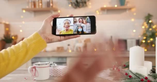 Närbild av smartphone-skärm med flera online videochatt med olika människor. Kvinna hand håller mobiltelefon talar på videosamtal med familj och blandras vänner på julafton i karantän — Stockvideo
