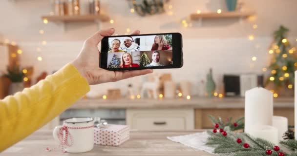 Primo piano dello schermo dello smartphone con più chat video online con diverse razze miste persone. La mano di donna tiene il cellulare che parla in videoconferenza con amici durante Anno nuovo. Concetto di Natale — Video Stock